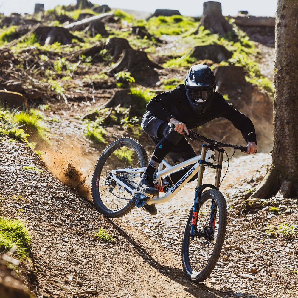 Person riding a mountain bike on a dirt trail with trees and rocks in the background
