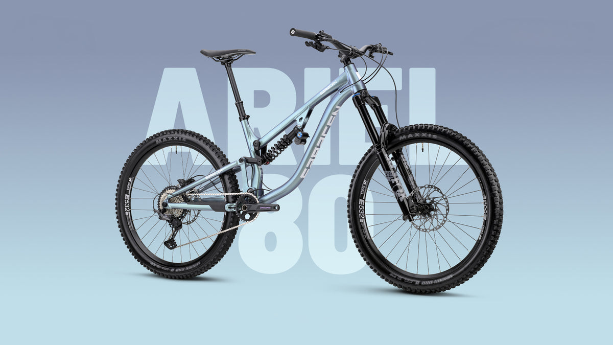 A full-suspension mountain bike with a metallic silver frame and black components, shown against a light blue gradient background with a large translucent 'APR 80' text overlay.