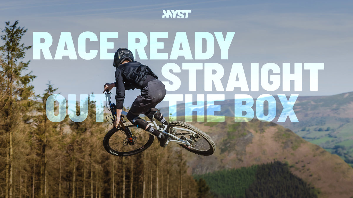 A mountain biker in black riding gear is airborne over a forested mountain landscape, with large overlaid text reading 'RACE READY STRAIGHT OUT OF THE BOX' and a small 'Nyst' logo at the top.