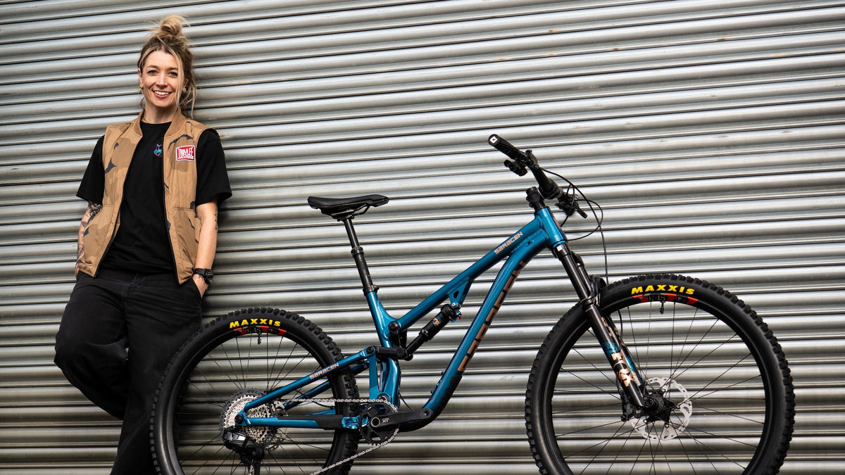 Person leaning against a blue bicycle with a corrugated metal wall in the background