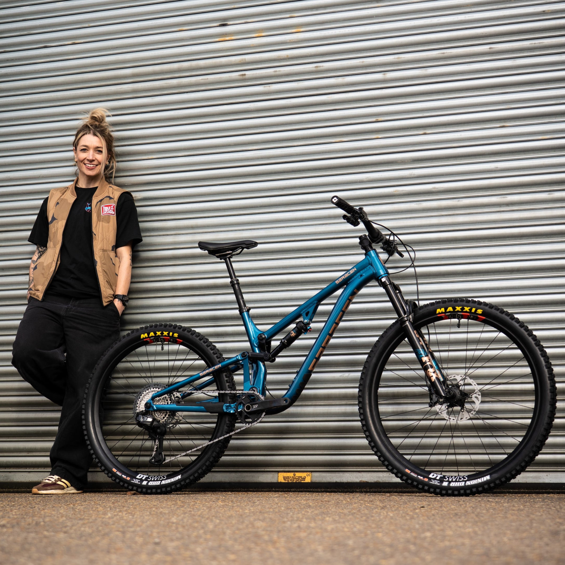 Woman standing next to a blue mountain bike in front of a metal shutter.