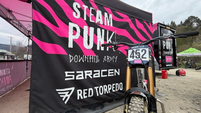 Bicycle with 'Steam Punk Downhill Army' and 'Saracen Red Torpedo' branding in front of a pink and black banner.