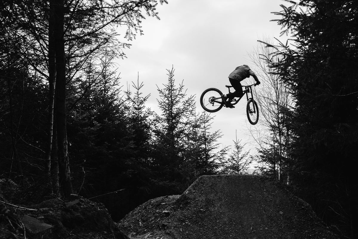 Person on a bicycle in mid-air over a dirt jump with trees in the background