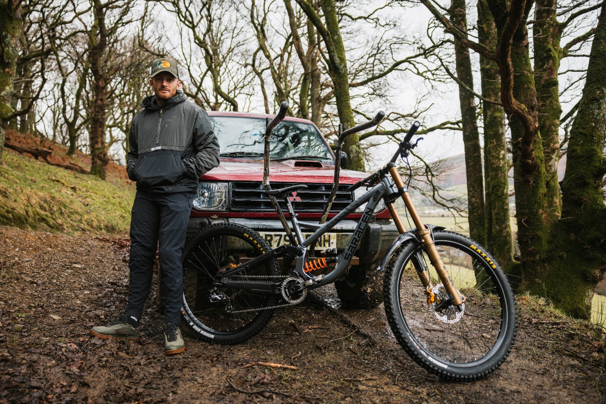 Man standing next to a red SUV with a mountain bike attached, in a forest setting.