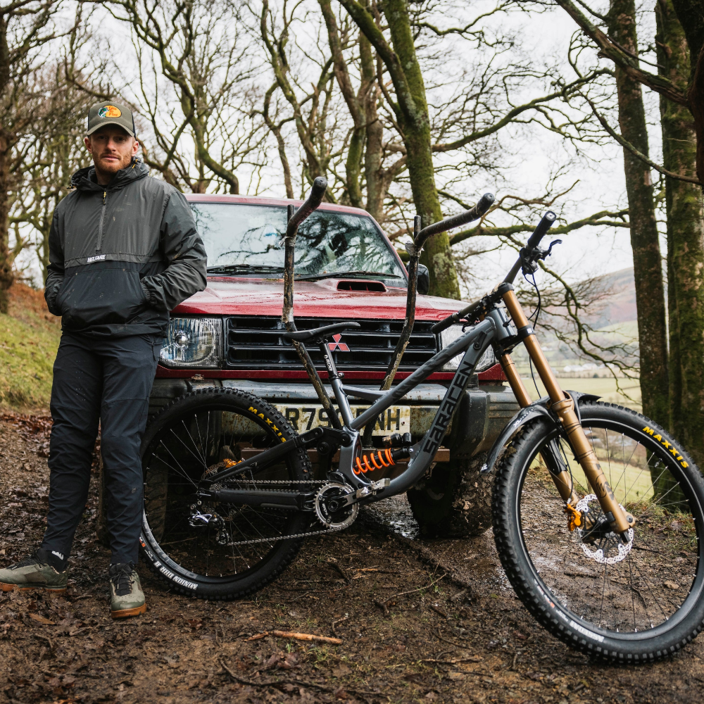 Man standing next to a red truck with a mountain bike in a forest setting