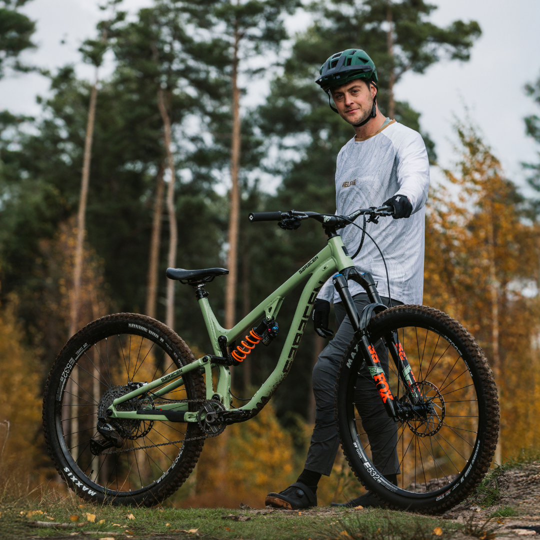 Person holding a green mountain bike in a forest setting