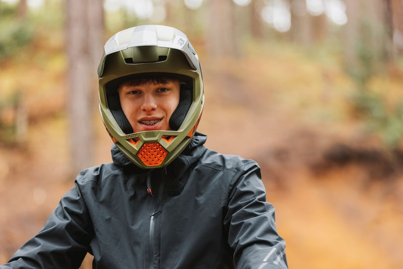 Person wearing a mountain bike helmet and black jacket in a forest setting.