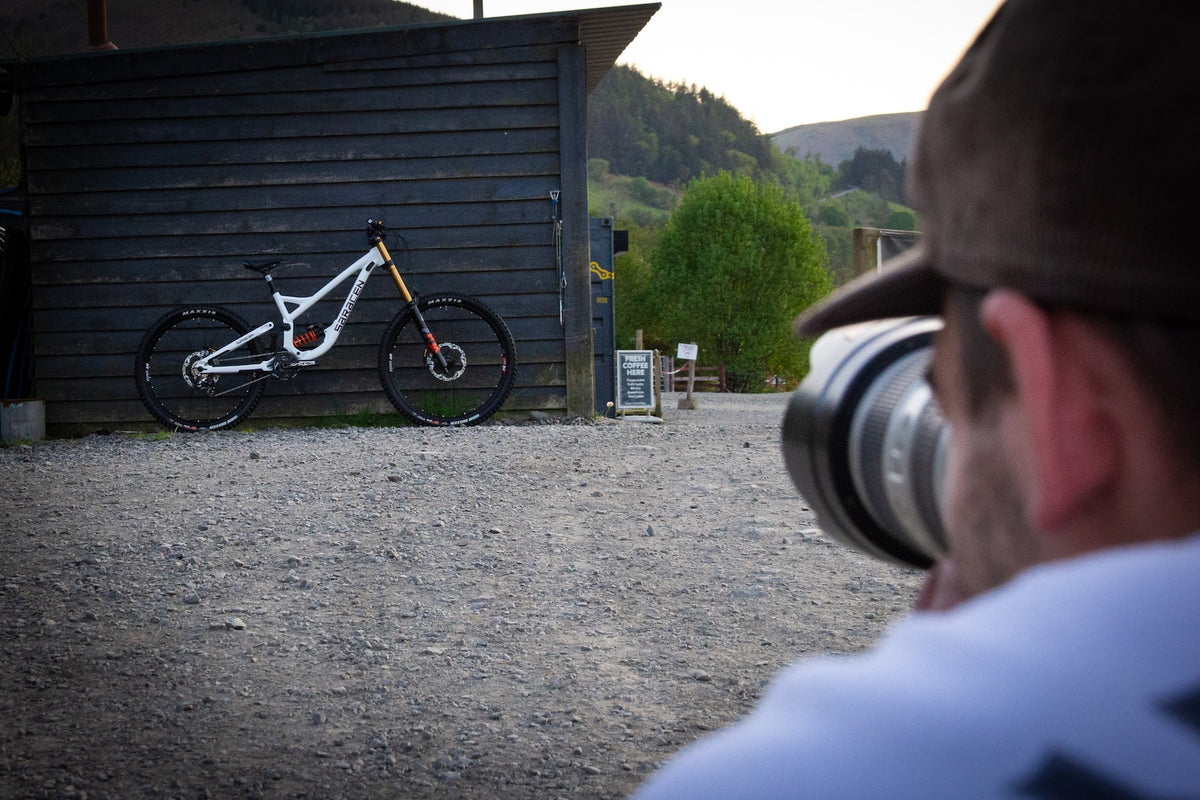 Person taking a photo of a mountain bike leaning against a wooden building.
