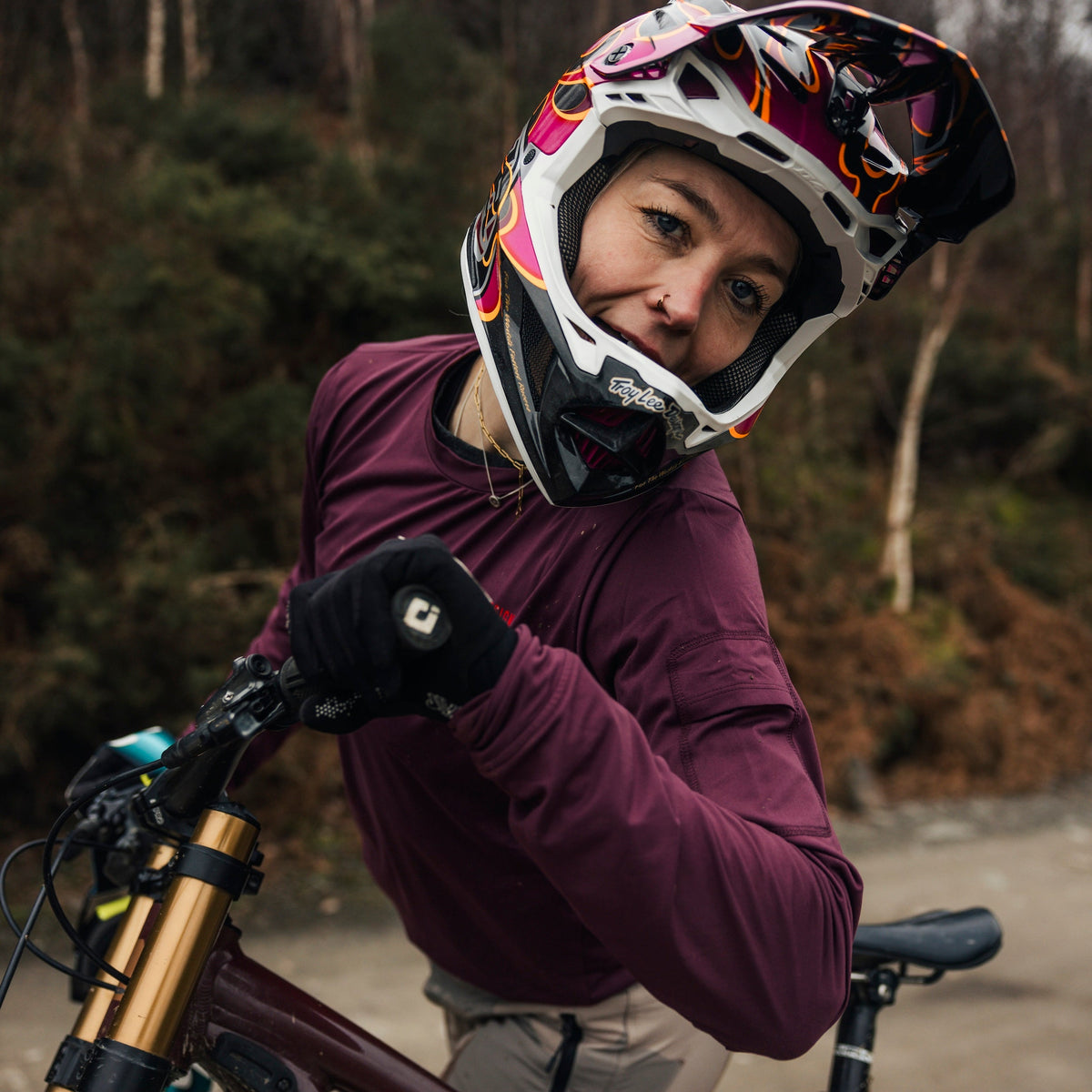 Person wearing a helmet and gloves, standing next to a bicycle in a forest setting