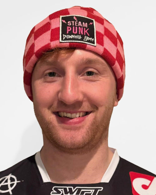 Person wearing a red checkered beanie with a patch and a black jacket with logos.