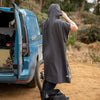 Person wearing a black rain poncho standing next to an open blue vehicle in a forested area.