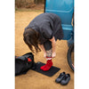 Person putting on red socks with a black mat and black shoes on the ground, next to a blue vehicle.