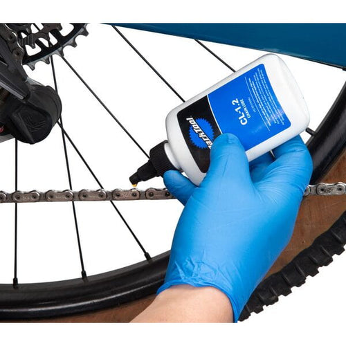 Person applying chain lube to a bicycle chain with a gloved hand